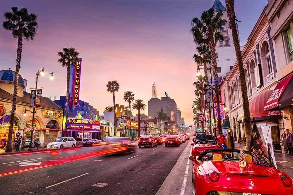 A street with cars and palm trees Description automatically generated